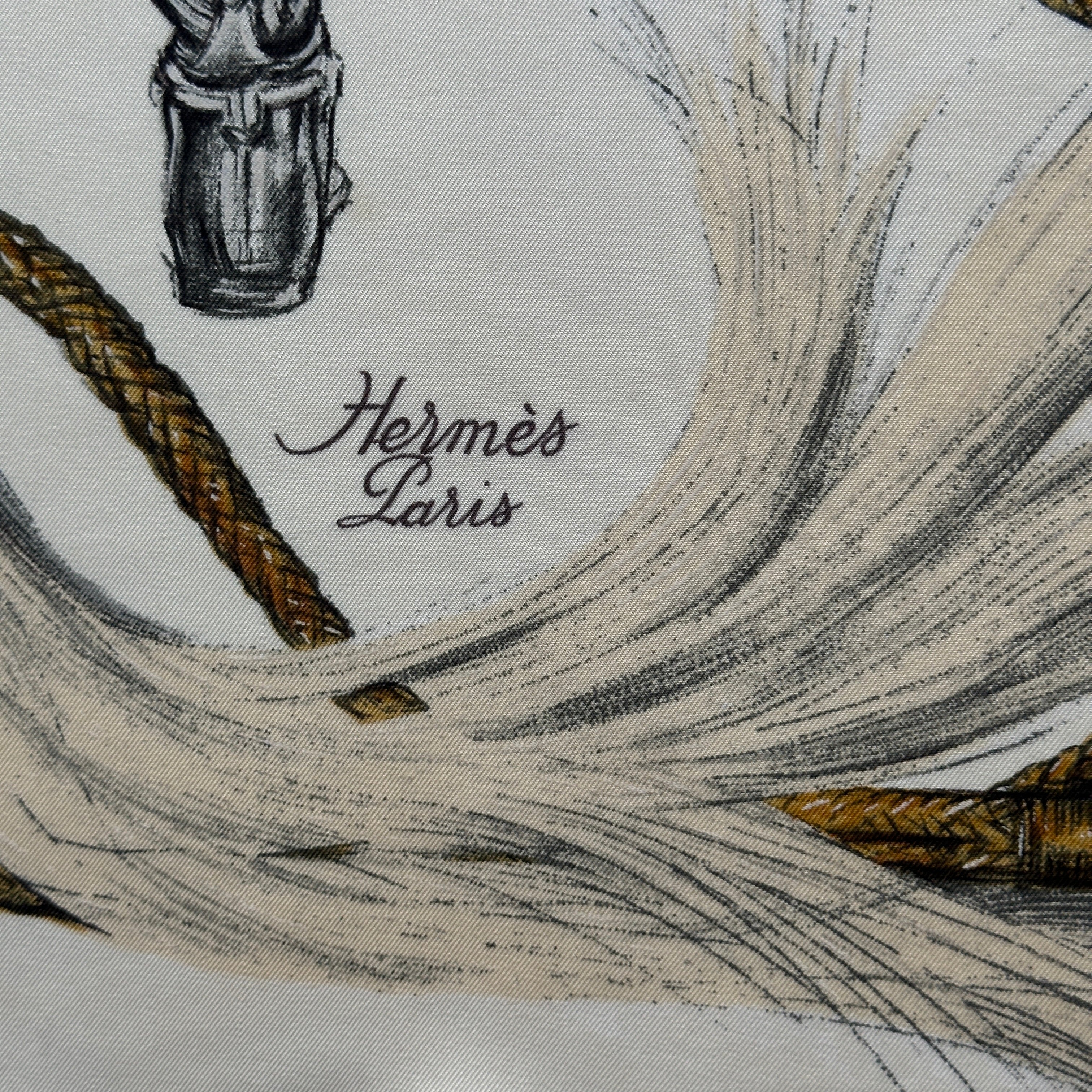 Signature "Hermès Paris" calligraphiée en noir près d'une botte cavalière, détail de la trame de soie.