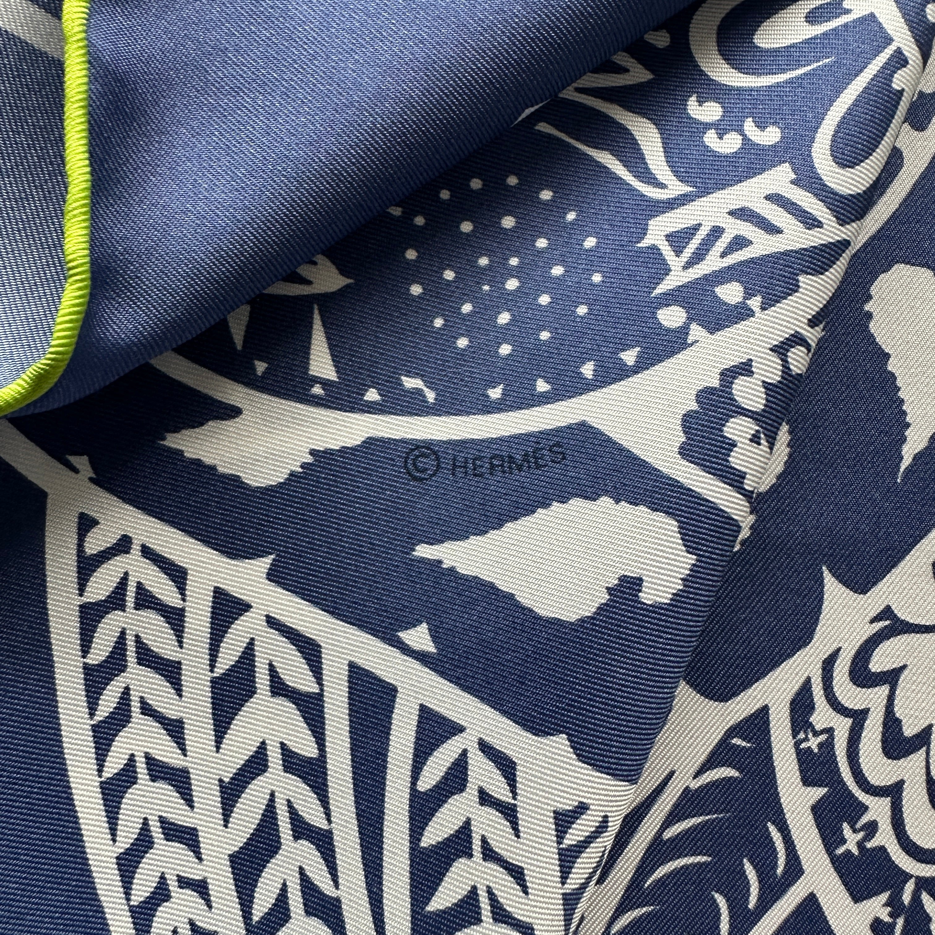Détail du motif sur la partie bleu marine du foulard Hermès, montrant le symbole de copyright "© HERMÈS" discrètement intégré dans le dessin.